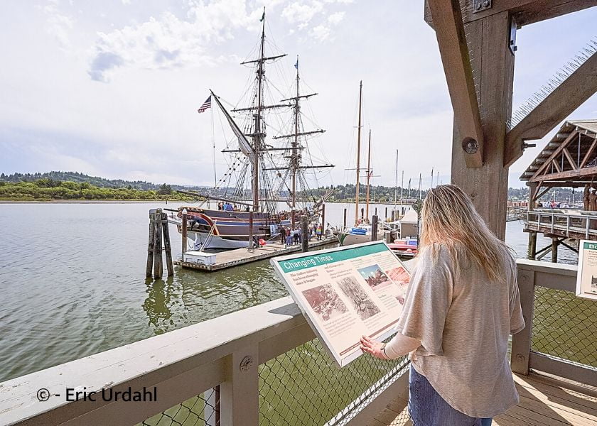 Tall Ships in the water at Coos Bay with girl reading information board.