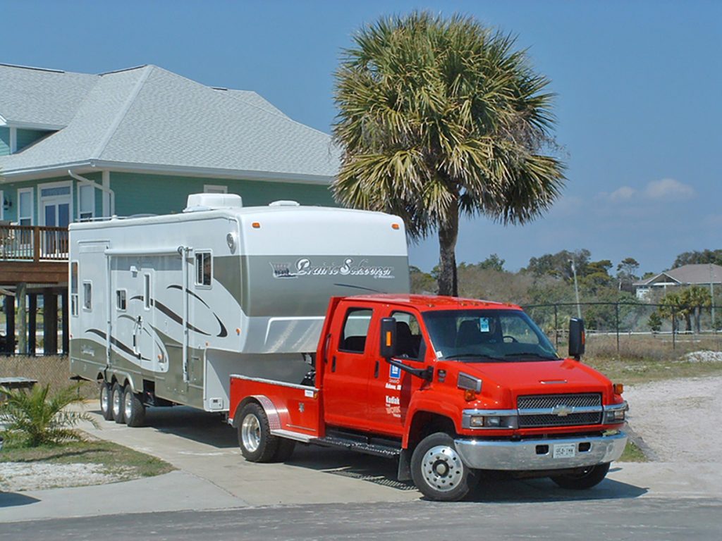 Red truck and trailer backing into a driveway