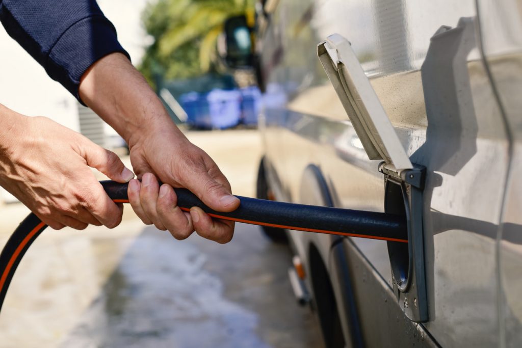 Hands attaching a water line to an RV