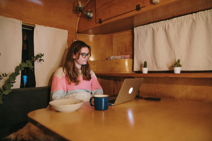 Young woman using a laptop and having dinner inside a vintage camper trailer