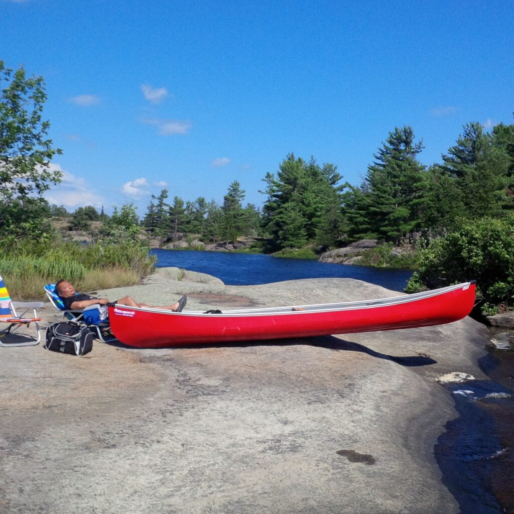 John Kim relaxing next to his canoe on a rock by the water