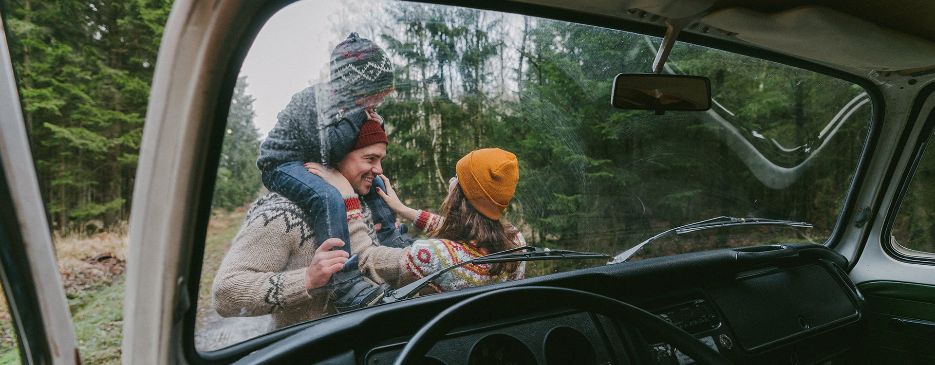 Father, mother, and child standing in front of their RV in a forest during winter time