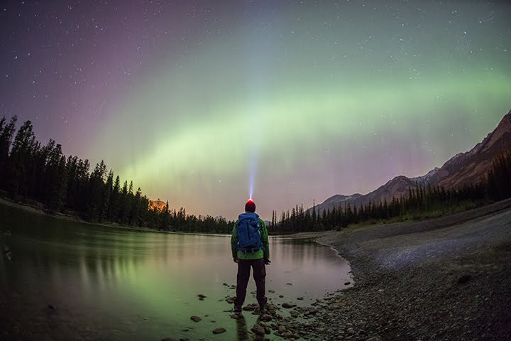 A man using his headlamp and looking at the night's sky and northern lights.