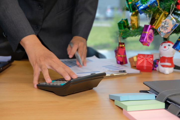 A financial adviser working on calculating a budget with calculator at an office with holiday decorations behind.