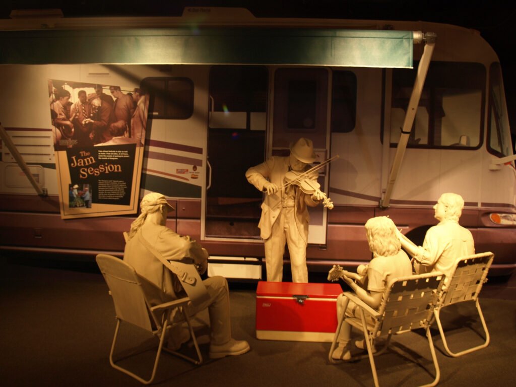 Statues playing music at a music jam in front of an RV at the International Bluegrass Music Museum.