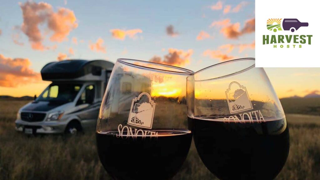 Two glasses of wine in front of an RV with a Harvest Hosts logo