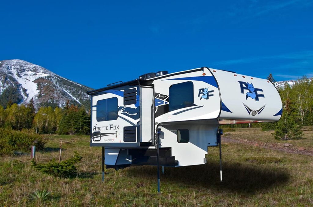 Exterior view of an Arctic Fox RV in a field in front of a mountain. 