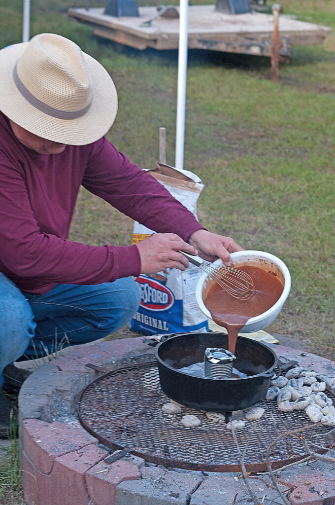 Man pouring chocolate cake ingredients around a tin can inside a Dutch oven