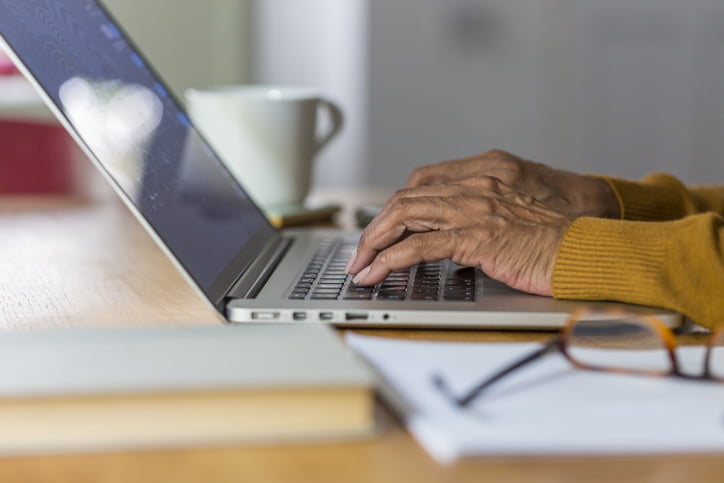 Hands of a senior African American woman sitting at the dining room table doing retirement finances on the laptop computer