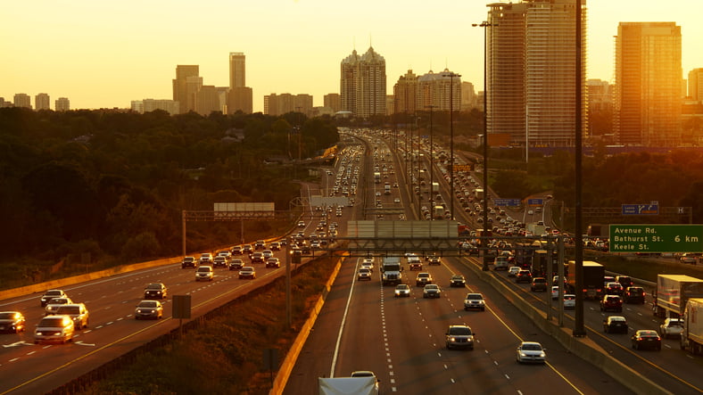 Cars driving in a restricted towing zone on the 401 Highway with Toronto city in the background.