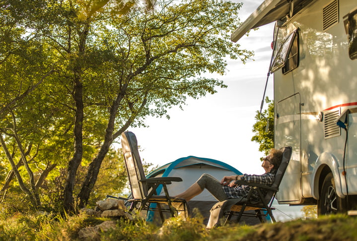 Woman sitting in a chair by an RV enjoying her vacation.