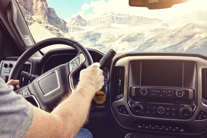 Man holding the steering wheel driving a truck on a rural road through the mountains