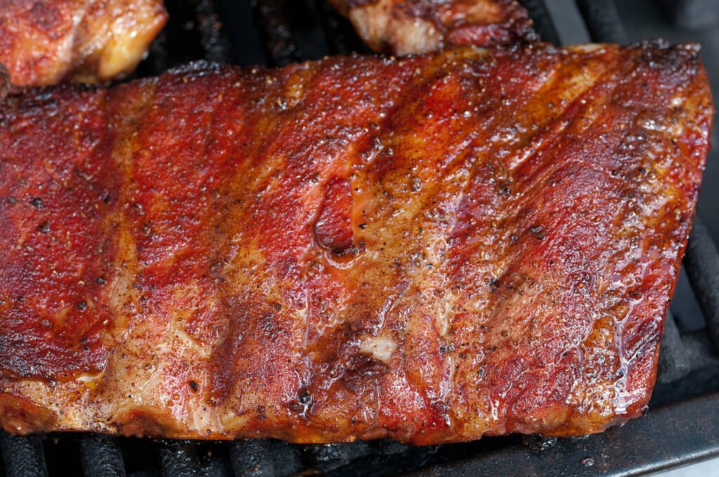 BBQ pork ribs on the grill covered in BBQ sauce.