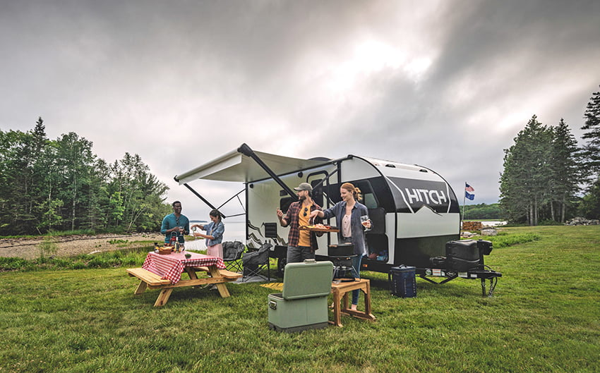 Two couples preparing food around a Cruiser RV Hitch travel trailer on a cloudy day