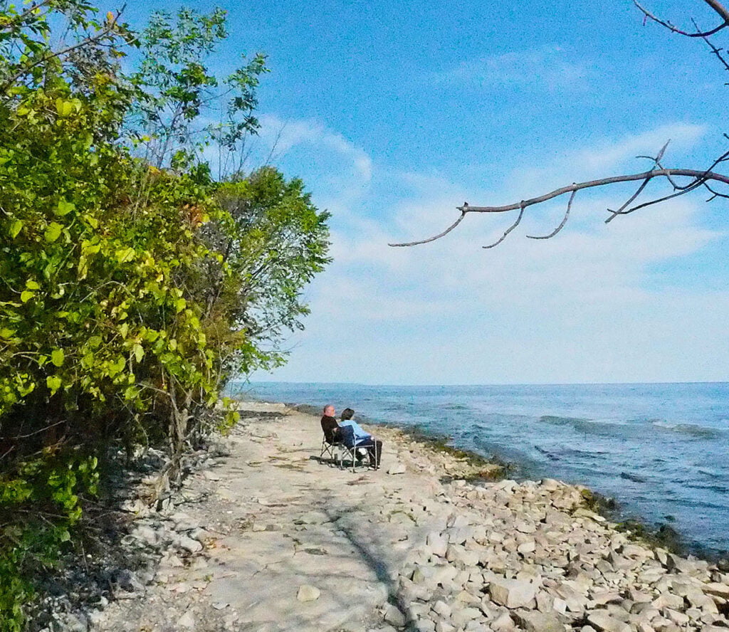 A man and woman sitting on the shoreline of South Georgian Bay in lawn chairs at Craigleith Provincial Park