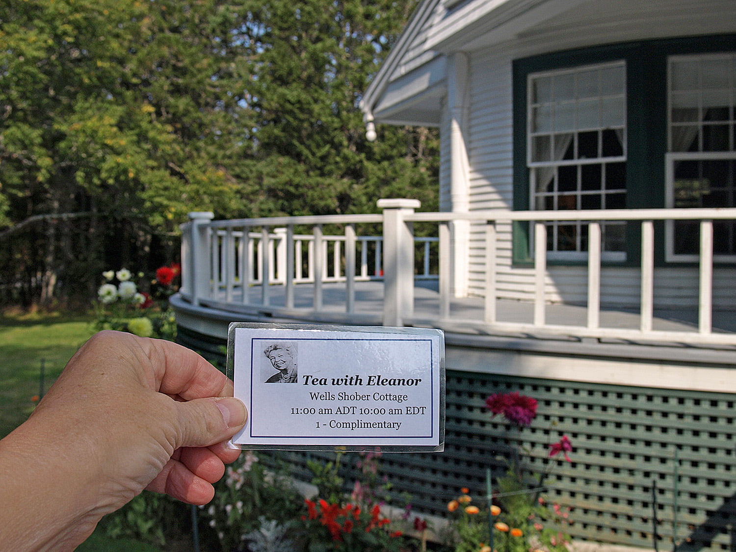 Hand holding ticket to Eleanor’s Tea in front of the historic Wells-Shober cottage.