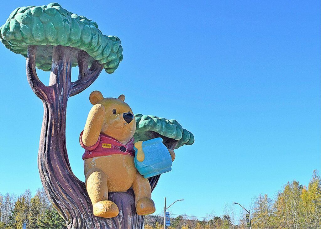 A statue of Winnie the Pooh sitting in a tree with a honey pot in White River, Ontario.