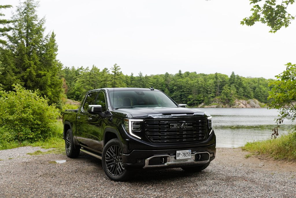 Exterior view of a black GMC Sierra Denali parked in front of a lake with trees in the background.