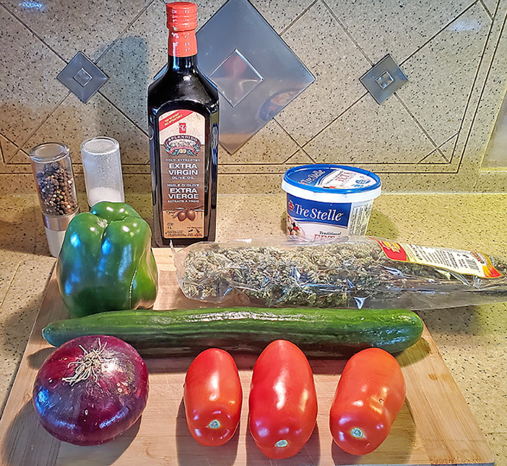 Cucumbers, red onion, tomatoes, green pepper, oregano, feta cheese, olive oil, salt and pepper are spread on a wooden cutting board, ready to make Greek Salad.