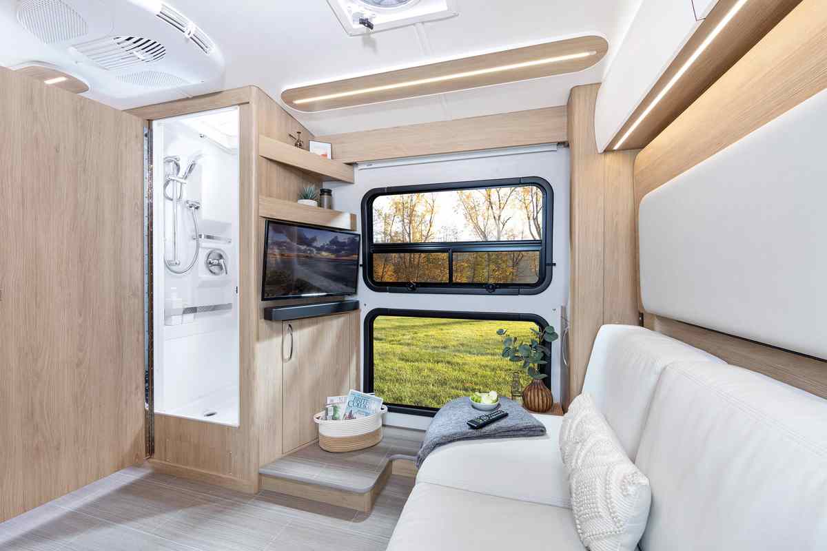 A white sectional sofa, entertainment system and two large expansive windows inside a Wonder Class B-Plus motorhome.