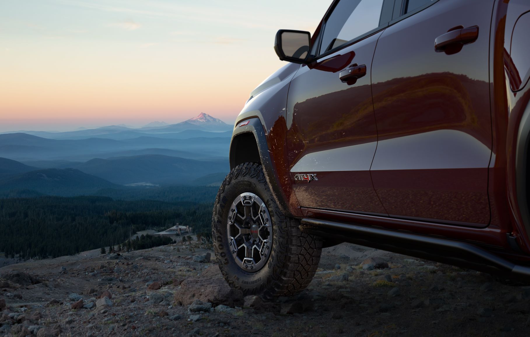 A red GMC Canyon AT4X is parked on rocky terrain looking out over a landscape of mountains fading off into the distance.