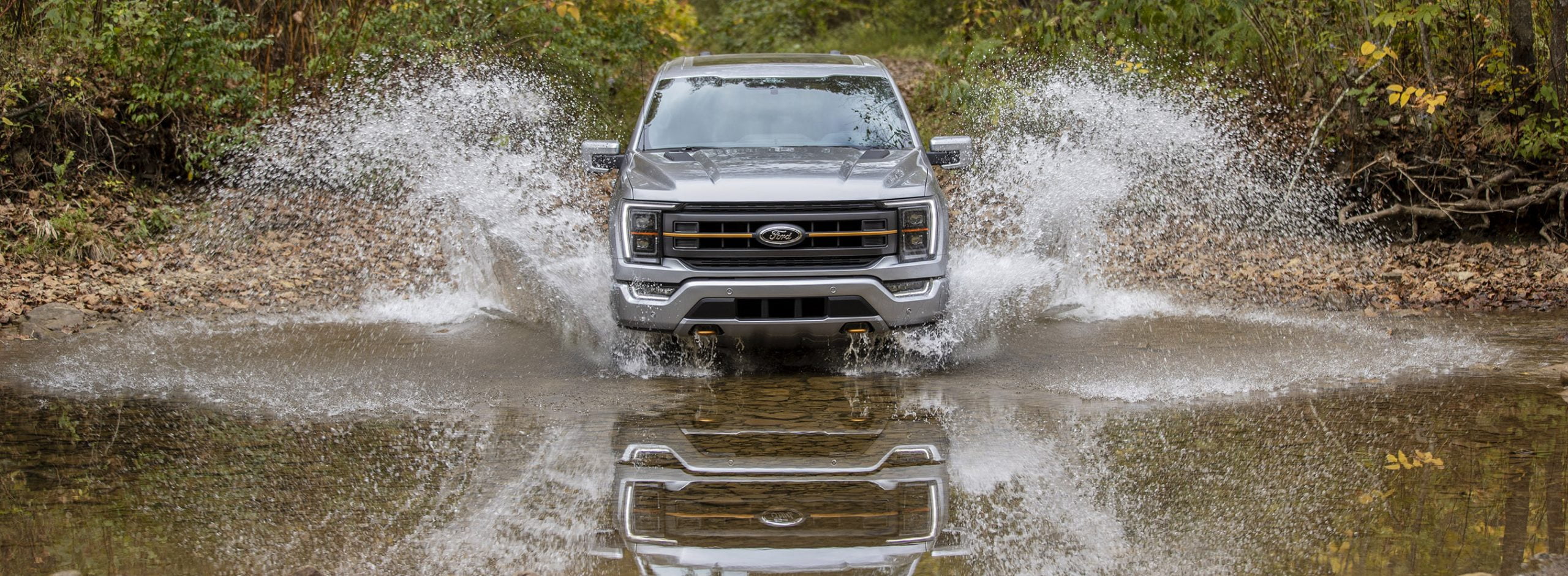 A 2021 Ford F-150 Tremor driving, head-on, through shallow water towards the viewer.