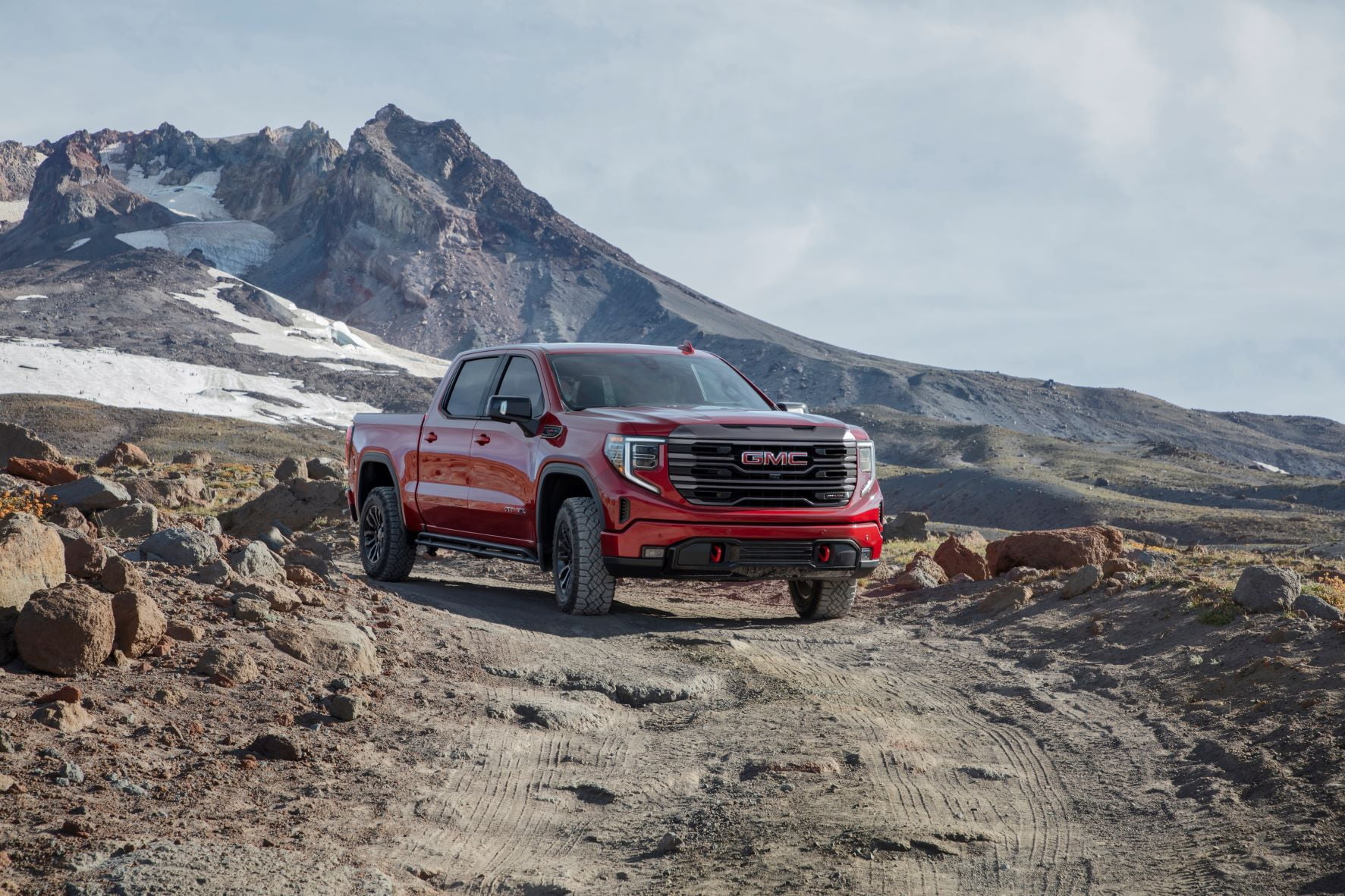 A red 2022 GMC Sierra AT4X-100 parked in front of rocky, snow-spotted, mountains.