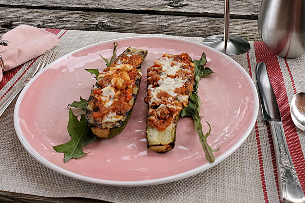 Two cooked zucchini boats sit atop fresh greens on a place-setting at a campground.
