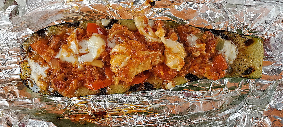 A grilled zucchini boat, fresh from the fire, sits on the foil wrap it was cooked in.