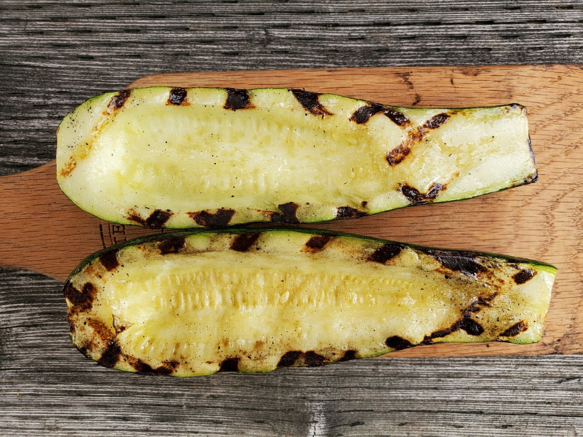 A hollowed out zucchini half with grill marks sits on a wooden cutting board.