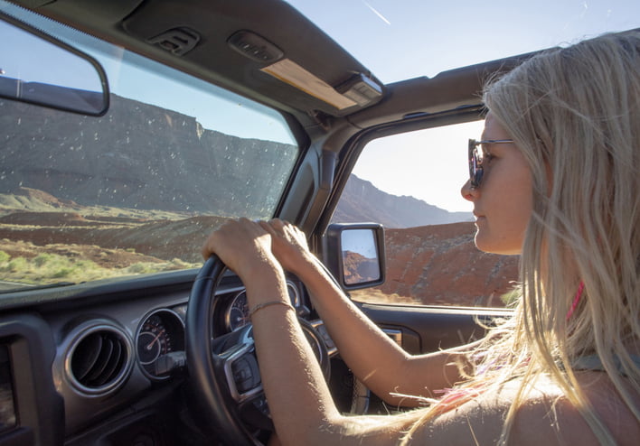 A young blonde woman driving her truck off-road through the desert.