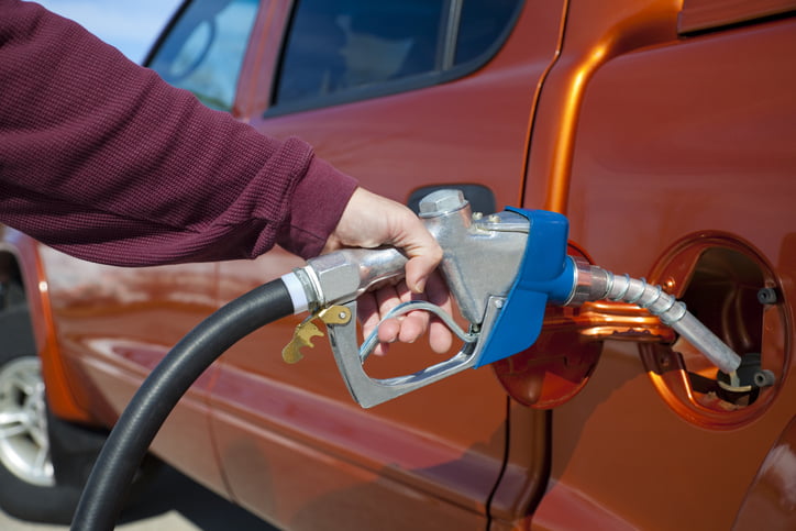 A large pick-up truck sparkles in the sun while its owner, mostly off camera, fills the gas tank.