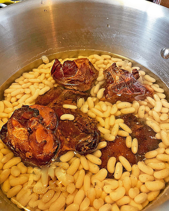 White kidney beans and ham hocks simmering in a stainless steel pot.