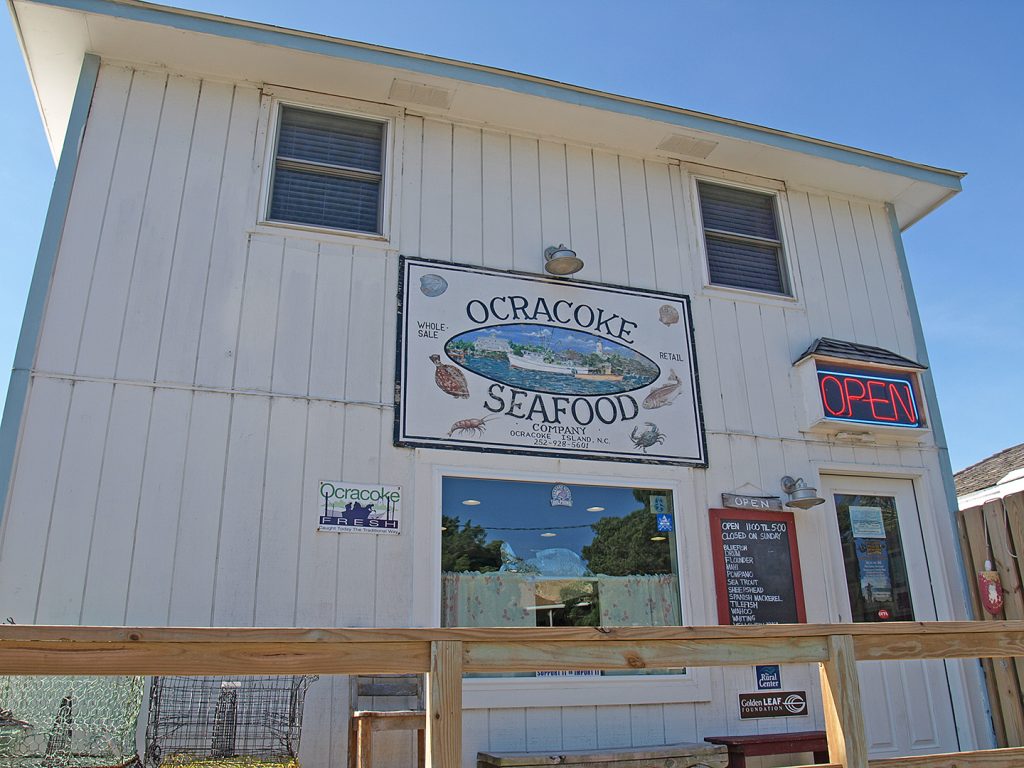 The exterior a building with white siding. The sign on the building reads, "Ocracoke Seafood."