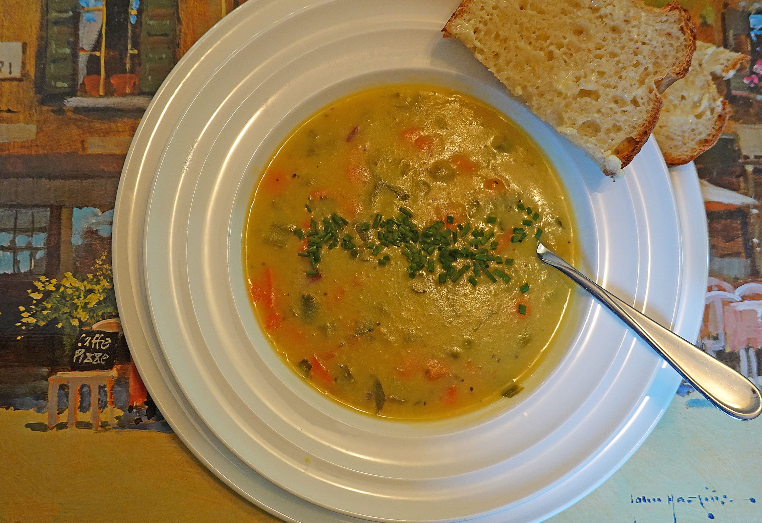 A bowl of white bean soup, garnished with parsley. A slice of whole wheat bread sits on the rim of the soup bowl.