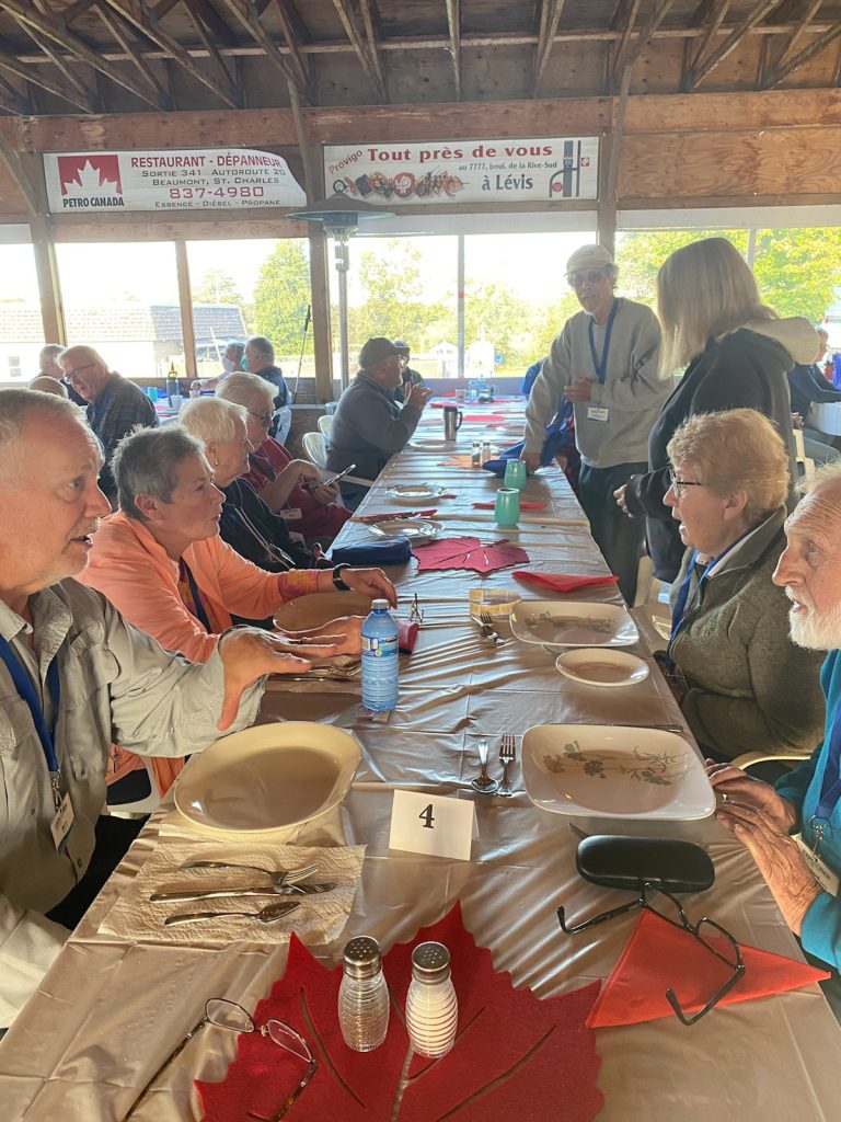 Many members of the Explorer RV Club seated at long tables in a dining hall before dinner. 