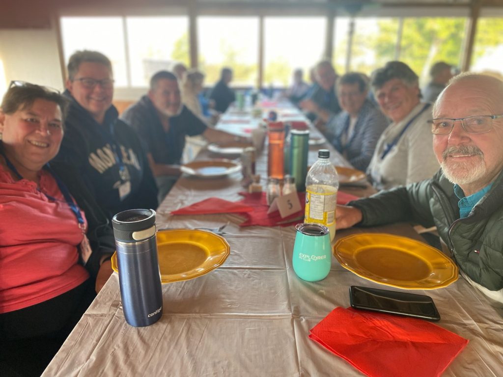 A group of people sitting at a long table in a dining hall. They are looking toward the camera and smiling.