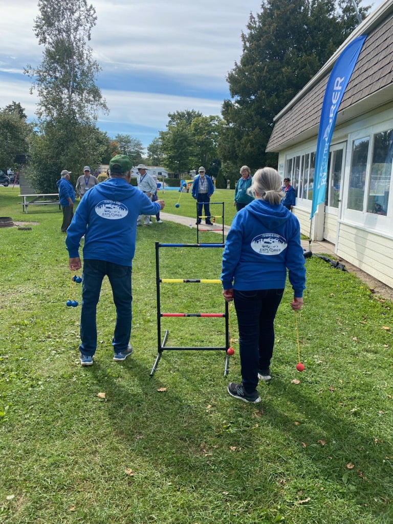 Several members of the Explorer RV Club wearing blue hooded sweaters that commemorate this year’s Rally outside playing ladder toss on a sunny day.