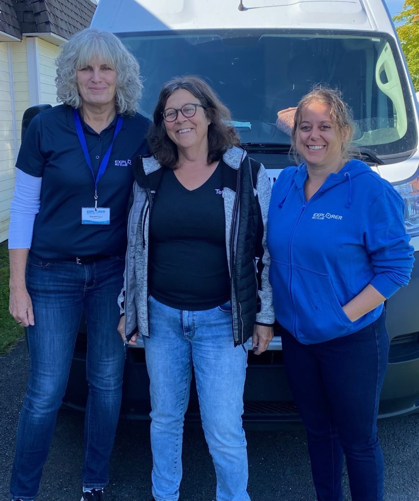 Three members of the Explorer RV Club and Terego teams pose, smiling, outside on a sunny day.