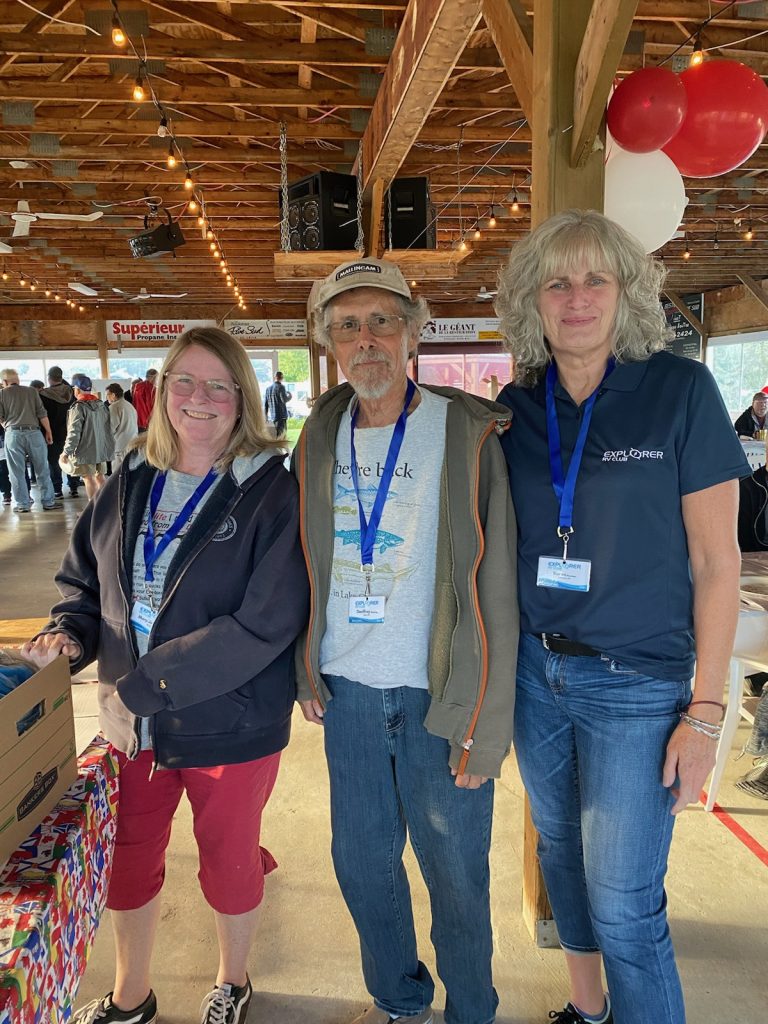 Three people posing arm in arm inside a dining hall. 