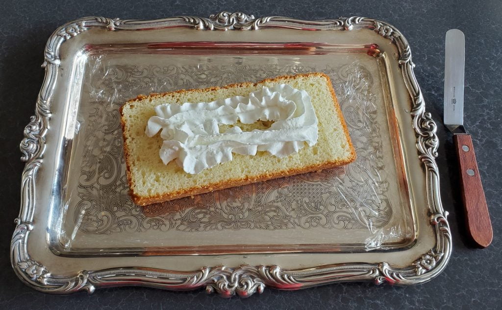 A piece of store-bought pound cake, sliced lengthwise, has two lines of whipped cream sprayed along the length of it.