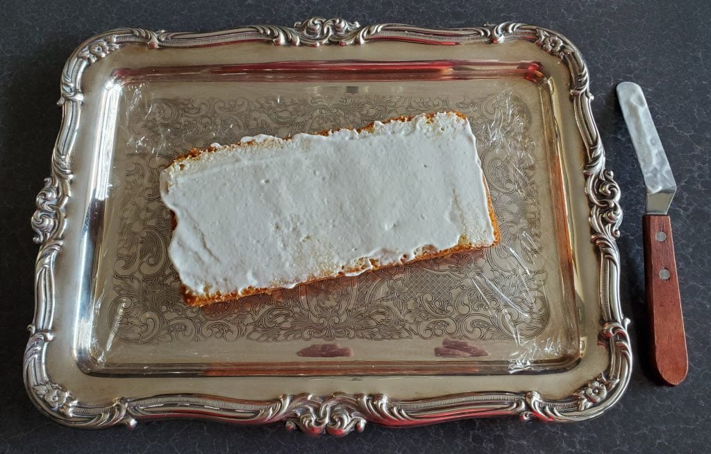 A piece of store-bought pound cake, sliced lengthwise, with whipped cream spread.