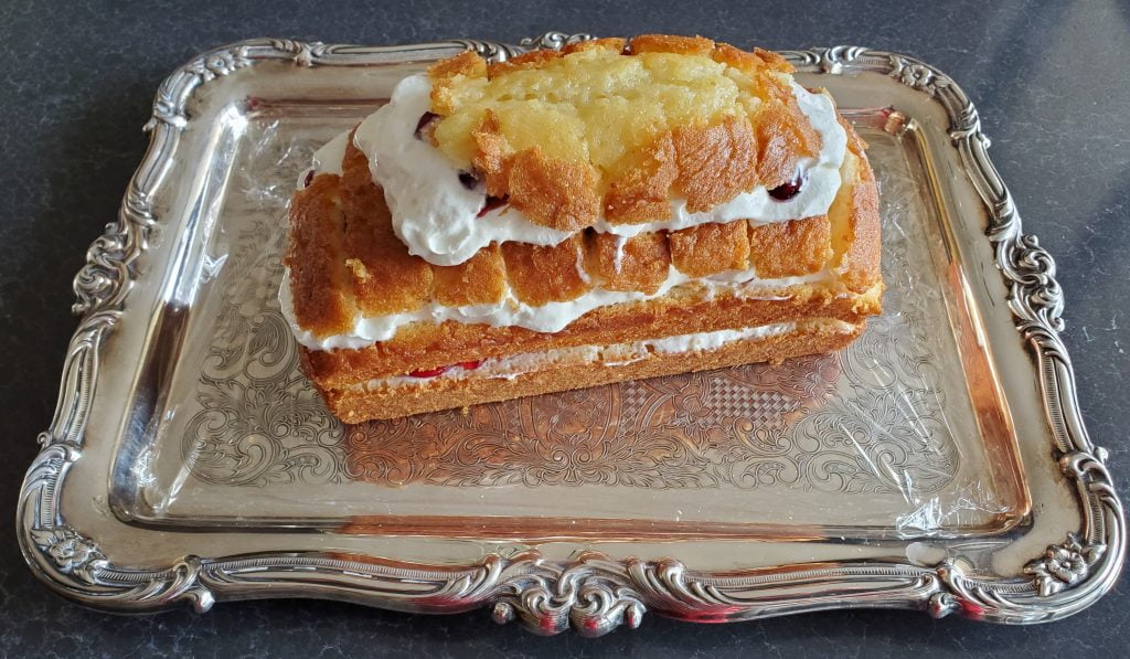 A Yule log beginning to take shape with four layers of pound cake, each with a layer of whipped cream, cherry pie filling, and another layer of whipped cream between them. 