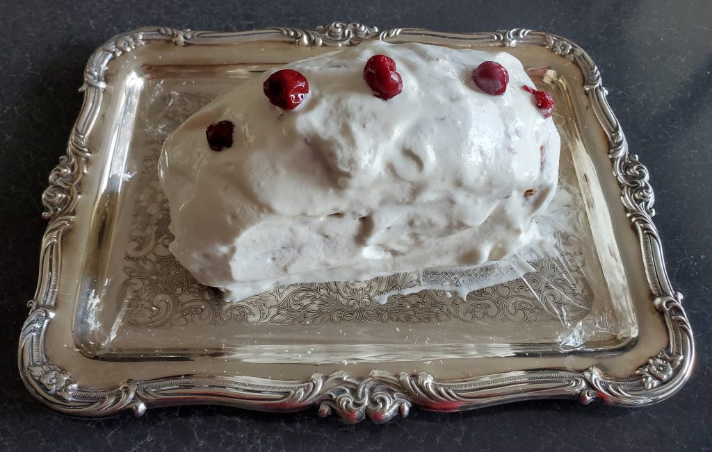 A Yule log covered in whipped cream with five cherries spaced evenly, lengthwise, along the top, presented on a silver serving tray.