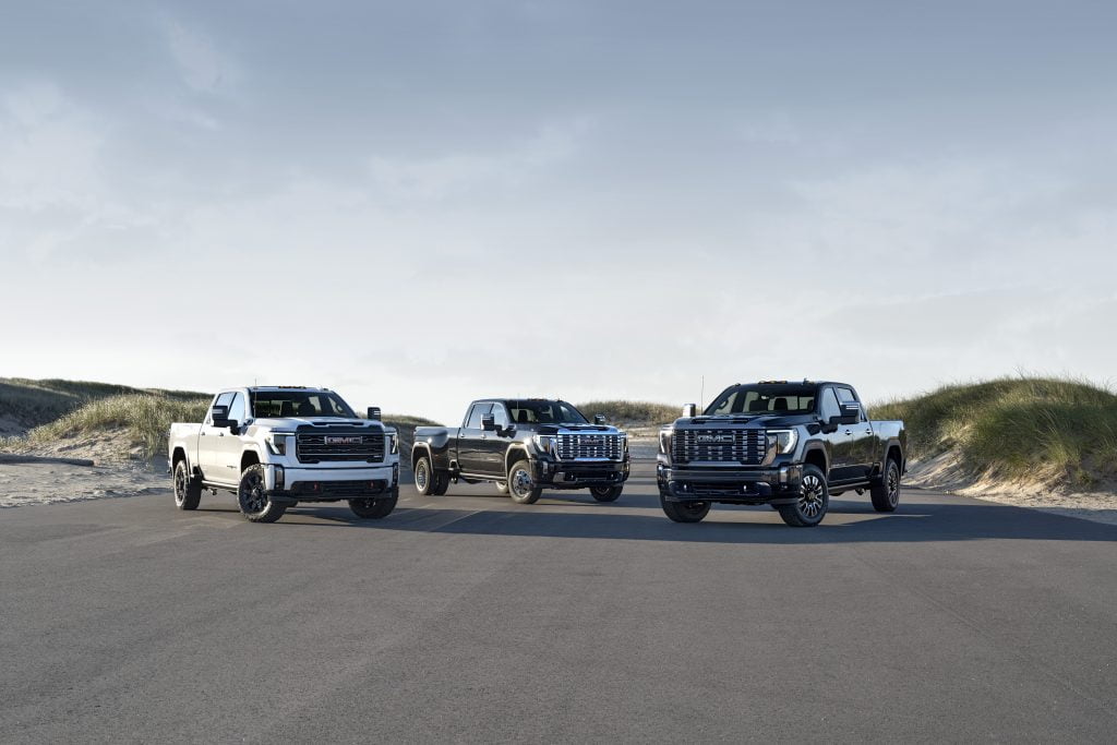 Three 2024 GMC Sierra Heavy Duty pick-up trucks are parked together, with the sun gleaming off of them.