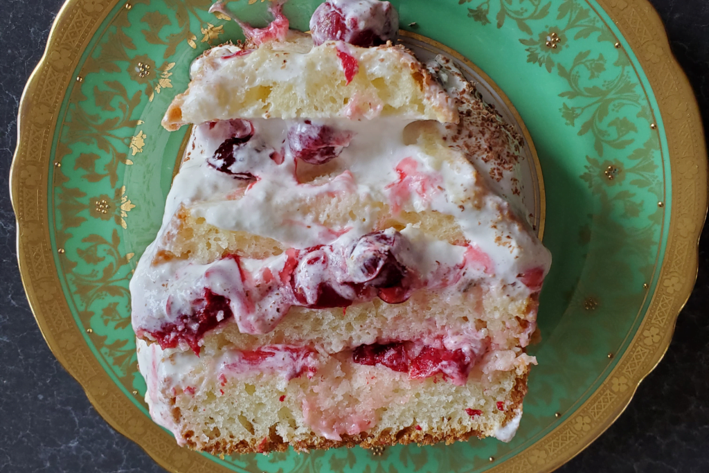 A slice of layered Yule log with cherries and whipped cream is presented on a green and gold dessert plate.