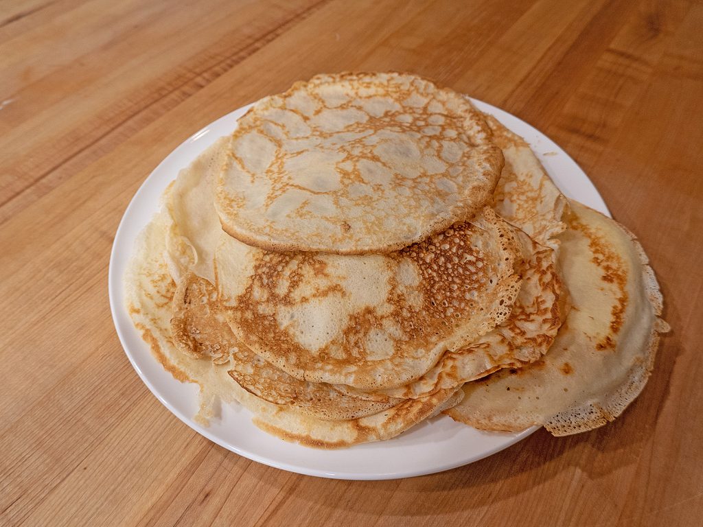 Pre-made, golden brown, crepes, stacked on a white plate.