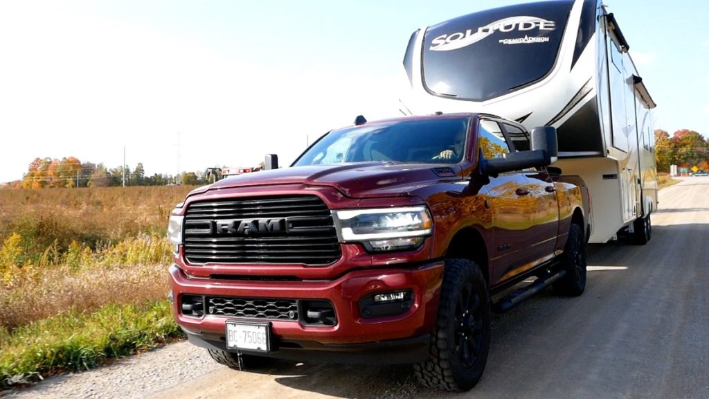 A red Dodge Ram truck pulling a Solitude 5th wheel motorhome behind it on a country road.