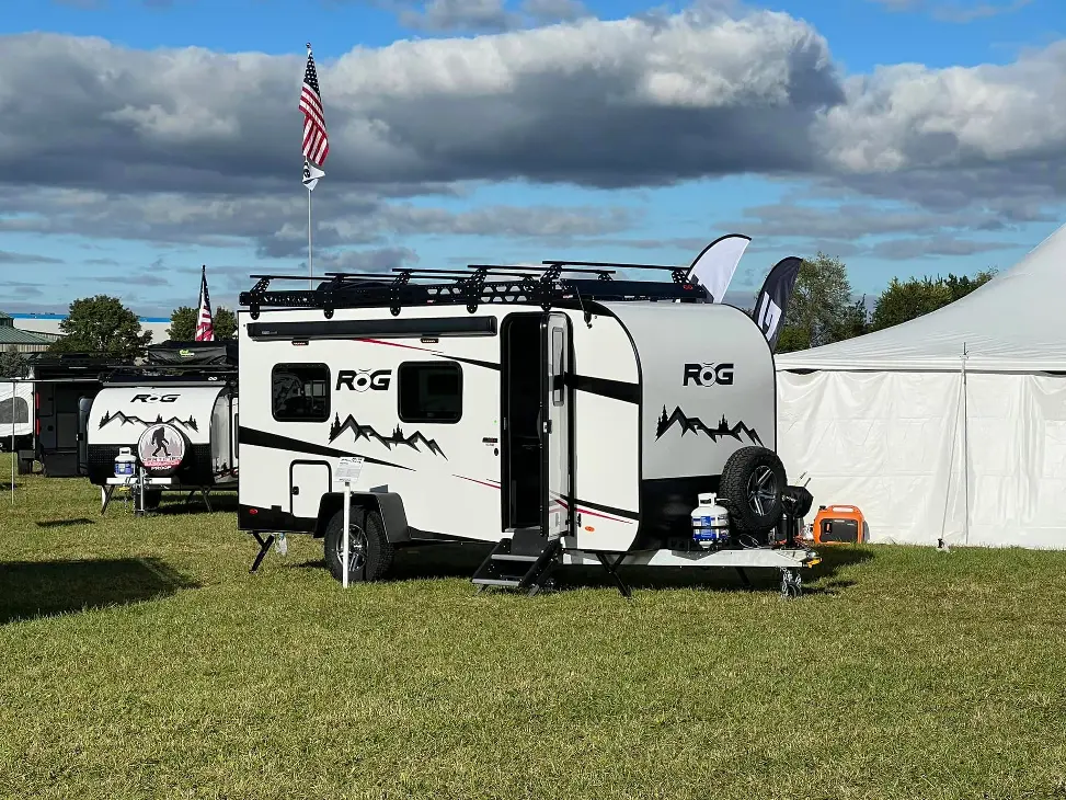 An RŎG 16RB by Encore RV parked on the grass on a sunny day, surrounded by other RVs.