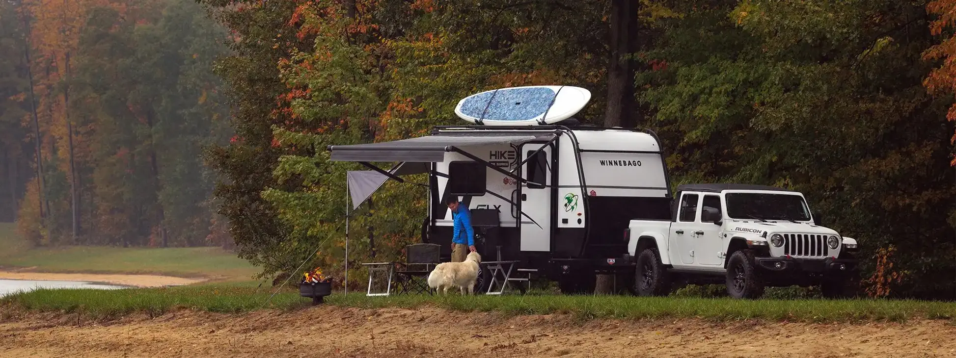 A man petting a dog outside his Winnebago HIKE parked off-grid in front of trees.